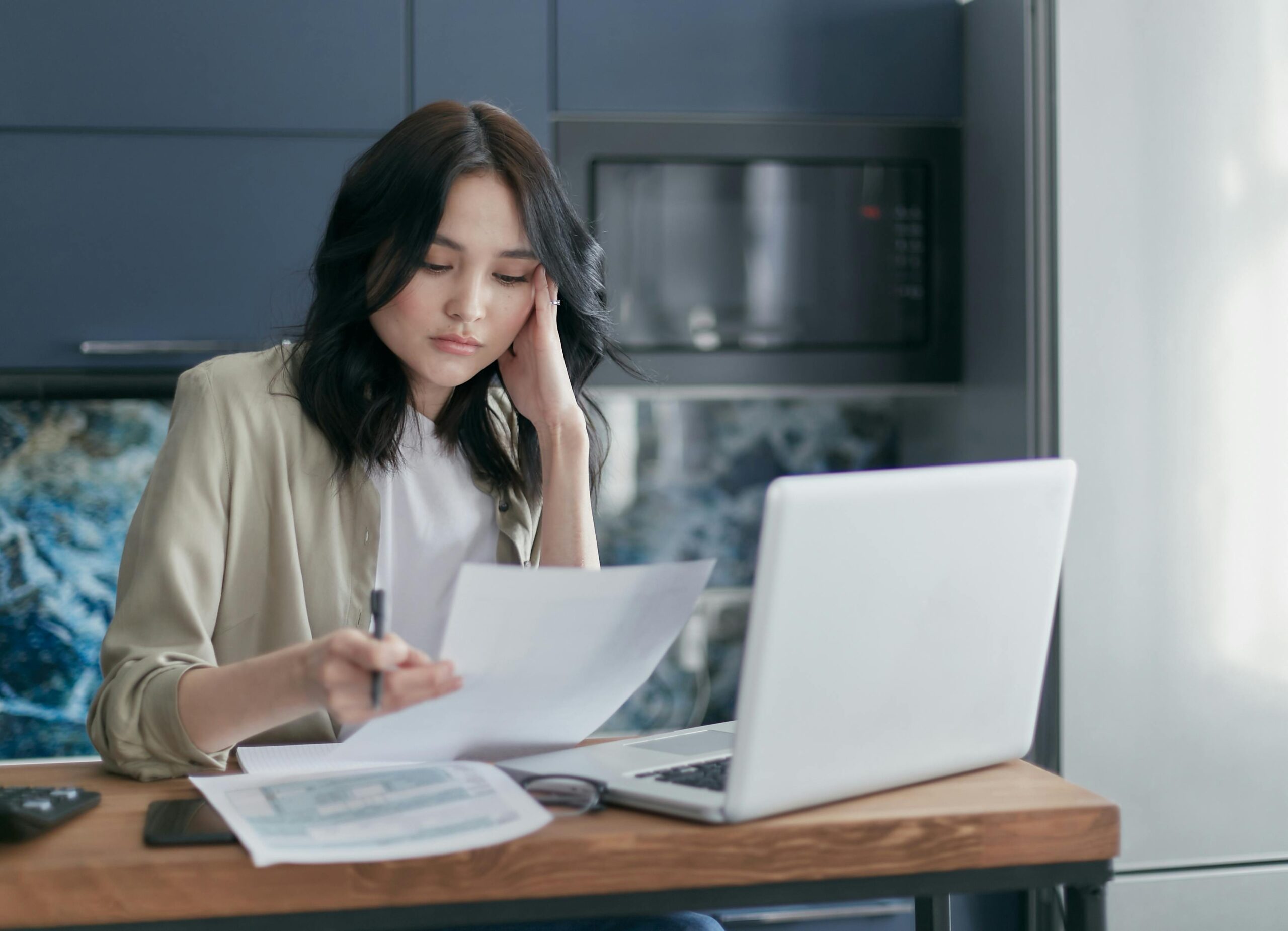 Focused young woman reviewing financial documents with a laptop in a home office setting.
